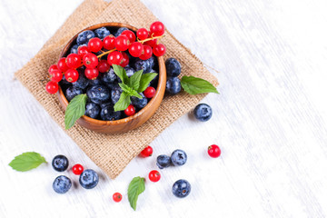 Fresh blueberries and red currants with mint leaves in a wooden bowl on burlap. Diet food, vegan berries