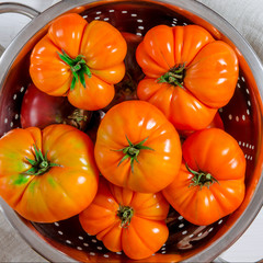 Washed various tomatoes in a colander on a wooden background