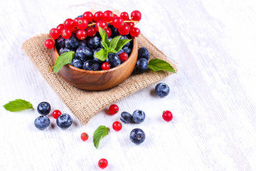 Fresh blueberries and red currants with mint leaves in a wooden bowl on burlap. Diet food, vegan berries