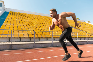 Image of shirtless sportsman running on track against stadium seats
