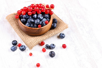 Fresh blueberries and red currants with mint leaves in a wooden bowl on burlap. Diet food, vegan berries