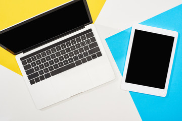 top view of laptop, digital tablet with blank screen on yellow, blue and white background