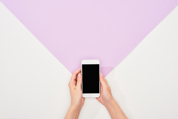 cropped view of woman holding smartphone on violet and white background