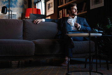Handsome young man holding coffee cup sitting on the couch in office