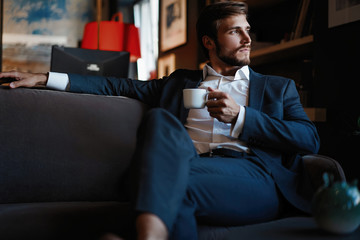 Handsome young man holding coffee cup sitting on the couch in office