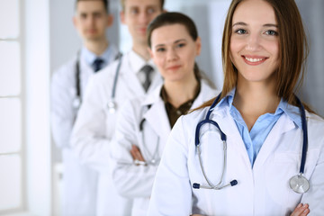 Fototapeta premium Doctor woman happy and cheerful while standing with colleagues in hospital office. Perfect medical service in clinic. Medicine and healthcare concept
