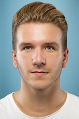 Obraz premium Caucasian young man's close up portrait on blue studio background. Beautiful male model with well-kept skin. Concept of human emotions, facial expression, sales, ad, beauty. Looks calm, looking up.