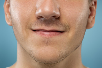 Obraz premium Caucasian young man's close up portrait on blue studio background. Beautiful male model with well-kept skin. Concept of human emotions, facial expression, sales, ad, beauty. Lips and cheeks.