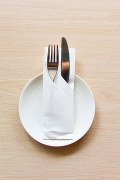 Knife and fork wrapped in a napkin lying on a white plate. The view from the top. The concept of the table setting.