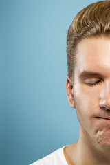 Caucasian young man's close up portrait on blue studio background. Beautiful male model with well-kept skin. Concept of human emotions, facial expression, sales, ad, beauty. Upset with eyes closed.