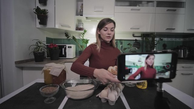 beautiful housewife-blogger writes a recipe food on smartphone for her subscribers on social networks during a live broadcast shows the necessary products to the camera, then drinks a glass of wine