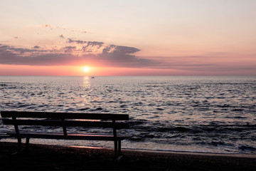 Beautiful sunset (sunrise) over the sea, beautiful waves and outlines of benches on the beach.