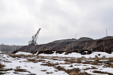 Obraz premium Piles of quartzite with a huge walking excavator and the remains of the forest in the background.