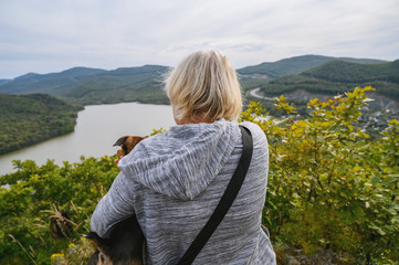 Fototapeta premium Dog owner and her pet looking in distance on top of the hill. View from back.