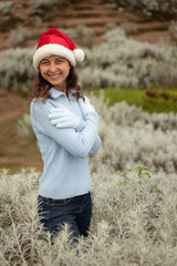 Young woman wearing red santa hat and blue gloves. Pretty Caucasian woman smiling and hugging herself. Christmas and New Year atmosphere.