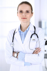 Doctor woman headshot at work in hospital. Physician standing straight and smiling, studio portrait. Medicine and health care concept