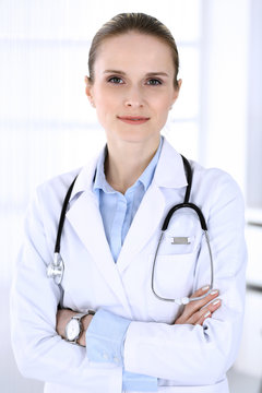 Doctor woman headshot at work in hospital. Physician standing straight and smiling, studio portrait. Medicine and health care concept