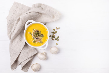 Bowl of Pumpkin and Mushrooms Soup with Cream and Pumpkin Seeds on Linen Napkin White Wooden Background Top View Copy Space