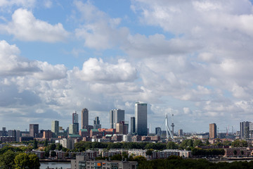 Downtown cityscape of the modern city of Rotterdam with high rise buildings, a neighbourhood, a river passing and dramatic clouds in the blue sky
