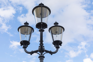 Fototapeta na wymiar Close-up of three black street lamps on one column against blue sky