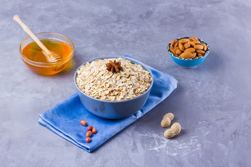 Dry oatmeal, nuts and honey. Oatmeal and almond nuts on cement background. Cereal and peanuts for healthy breakfast. Oatmeal in bowl on blue napkin