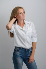 portrait of a young beautiful girl in a white shirt and jeans on a gray background