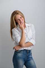 portrait of a young beautiful girl in a white shirt and jeans on a gray background