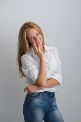 portrait of a young beautiful girl in a white shirt and jeans on a gray background