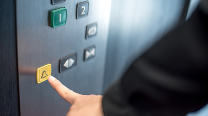 Male forefinger pressing on emergency stop and alarm button in elevator (lift). Mechanical...