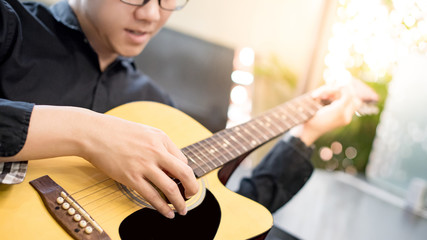 Young Asian man guitarist playing music with classic guitar at home. String musical instrument for recreational activity or personal hobby. Relaxation and entertainment concepts