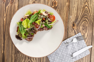 Spicy roastbeef Salad with green mix and tomato on white plate on wooden table