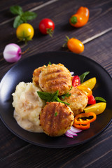 Fish cakes with mashed potatoes and vegetables, garnished with basil. Fish burgers on black table. Vertical image