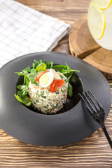 Russian traditional salad Olivier with egg and tomato on top on black plate on wooden table