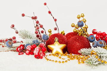 Vivid Christmas composition with baubles, holly berries, Xmas fir tree twig and golden garland on white snow background