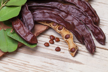 Carob. Organic carob pods with seeds and leaves on white wooden table. Healthy eating, food background.