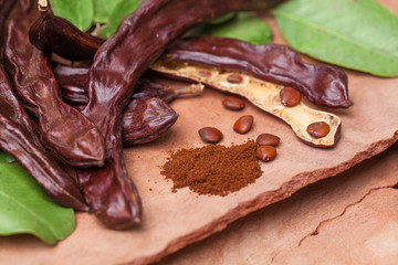 Carob. Organic carob pods with seeds and leaves on tree bark table. Healthy eating, food background.