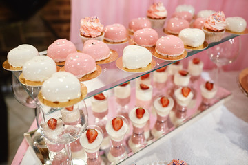 Wedding candy bar with pink and white deserts. Strawberry cupcakes, jelly and modern desserts.
