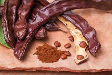 Carob. Organic carob pods with seeds and leaves on tree bark table. Healthy eating, food background.