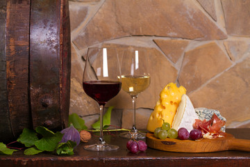 Red and white wine with  grapes, cheese, jamon, figs and nuts beside old cask in wine cellar. Room for text, copy space