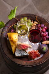Red and white wine with  grapes on old cask in wine cellar. Glasses and bottles of wine with cheese, jamon, figs and nuts. View from above, top view