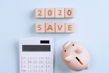 Abstract 2020 financial goal design concept - geometric wood blocks cubes on blue table background with piggy bank, top view, flat lay, copy space.