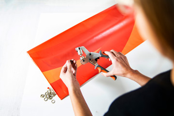 Advertising banner. The worker knocks out a hole in the banner and fixes the metal eyelets.