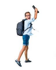 Full body of Student kid with backpack and glasses holding a book and jumping on isolated white background