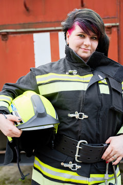 Image of young brunette fireman with helmet in her hands on background of fire engines