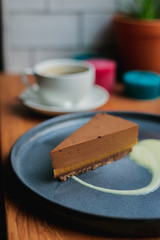 A piece of chocolate banana cheesecake with vanila sauce on a blue plate, white cup of coffee