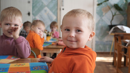Little cute boy sitting at table and smiling in kindergarden