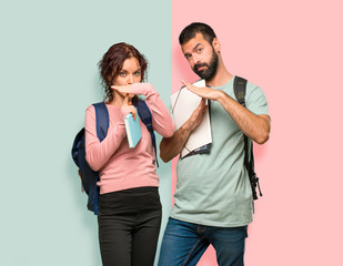 Two students with backpacks and books making stop gesture with her hand to stop an act on colorful wall