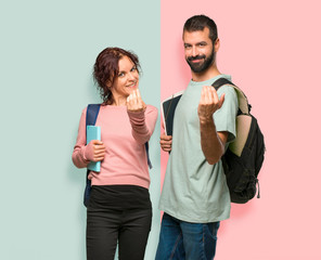 Two students with backpacks and books presenting and inviting to come with hand on colorful wall