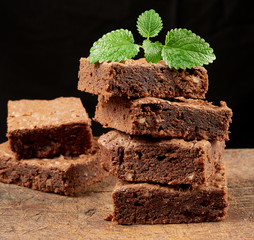stack of baked square pieces of chocolate brownie cake on brown wooden cutting board