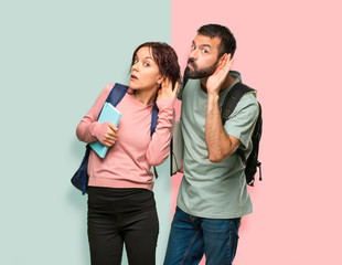 Two students with backpacks and books listening to something by putting hand on the ear on colorful...